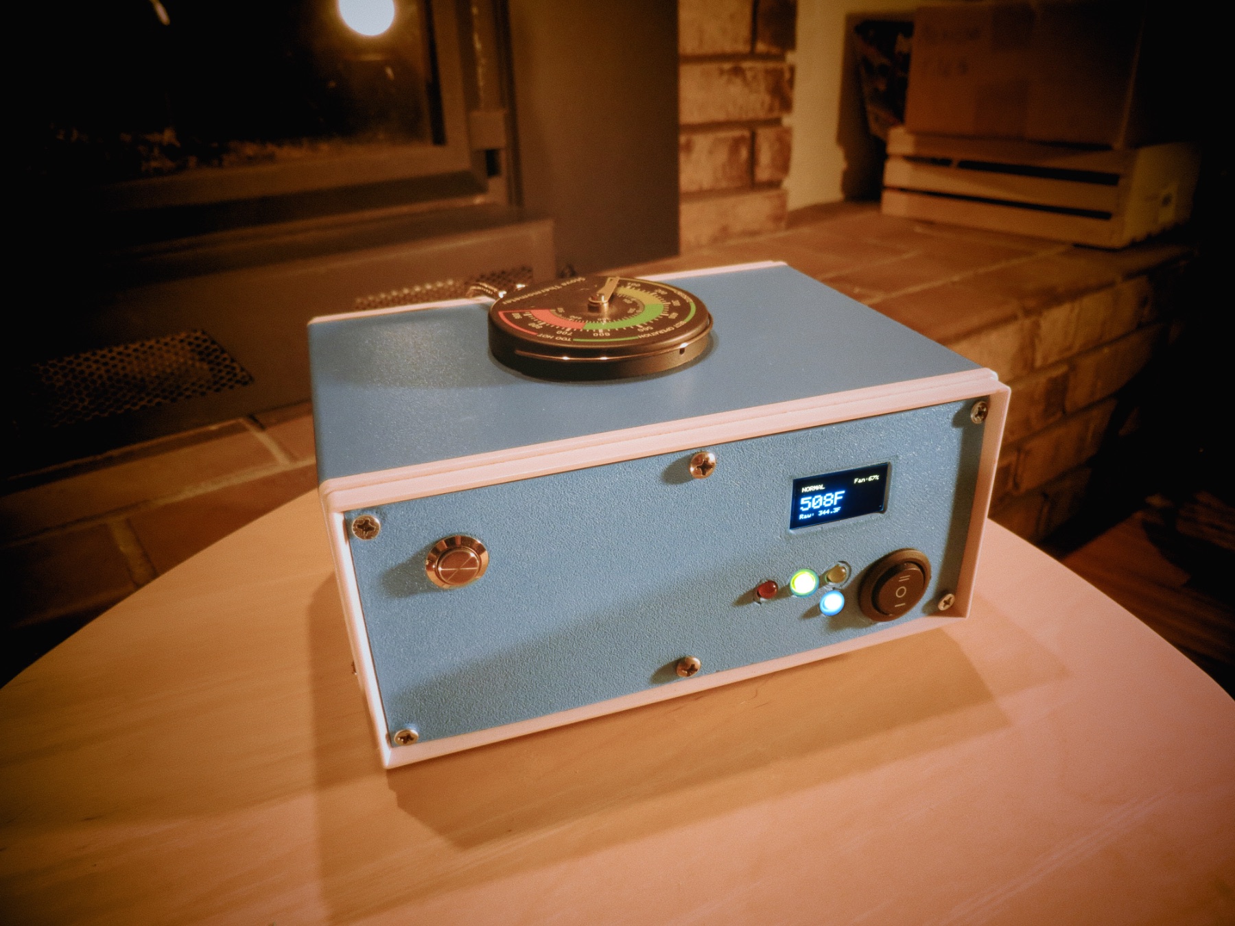 stoveLogic in firelight on a maple table, analog thermometer resting on top, OLED glowing