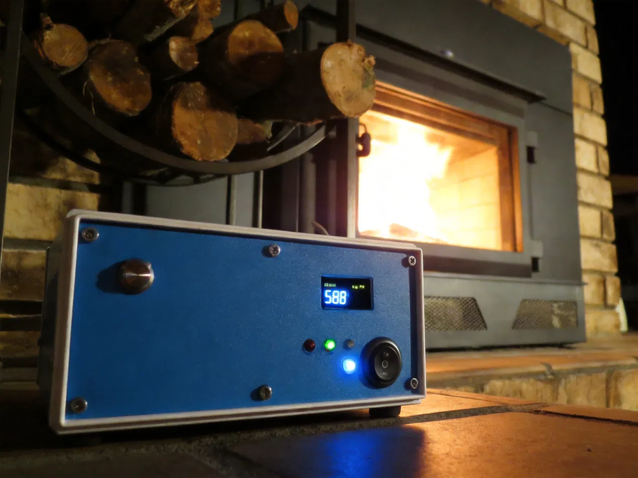 stoveLogic in front of a blazing wood stove at night, blue LED glowing, OLED lit