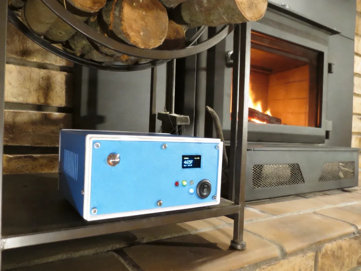 stoveLogic sitting on the hearth in front of a working wood stove, OLED reading 465°F